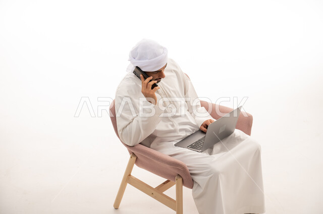 بورتريه لرجل عربي خليجي اماراتي يجلس على كرسي يستخدم جهاز الحاسوب، إجراء مكالمات هاتفية ، تواصل اجتماعي، محادثات ودردشة، التواصل مع الأصدقاء، اجتماع عمل عن بعد ،  خلفية بيضاء .