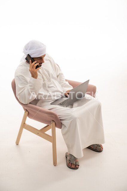 بورتريه لرجل عربي خليجي إماراتي يجلس على كرسي يستخدم جهاز الحاسوب، اجراء مكالمات هاتفية ، اجتماع عمل عن بعد ،  تواصل اجتماعي، محادثات ودردشة، التواصل مع الأصدقاء،  خلفية بيضاء .
