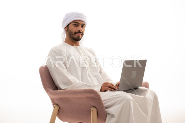 بورتريه لرجل عربي خليجي إماراتي يجلس على كرسي يستخدم جهاز الحاسوب، اجراء مكالمات فيديو، تواصل اجتماعي، محادثات ودردشة، التواصل مع الأصدقاء، اجتماع عمل عن بعد،  تصفح الانترنت ، خلفية بيضاء .