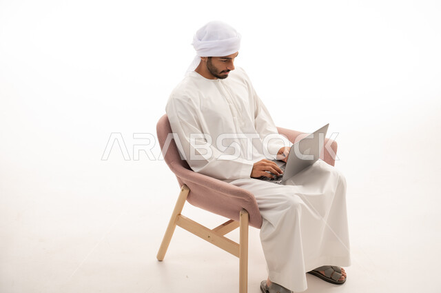بورتريه لرجل عربي خليجي إماراتي يجلس على كرسي يستخدم جهاز الحاسوب، اجراء مكالمات فيديو،  محادثات ودردشة، تواصل اجتماعي ، التواصل مع الأصدقاء، اجتماع عمل عن بعد،  تصفح الانترنت ، خلفية بيضاء .