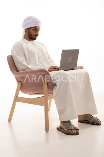 بورتريه لرجل عربي خليجي إماراتي يجلس على كرسي يستخدم جهاز الحاسوب، تواصل اجتماعي، محادثات ودردشة، التواصل مع الأصدقاء، اجتماع عمل عن بعد،  تصفح الانترنت ، اجراء مكالمات فيديو،  خلفية بيضاء .