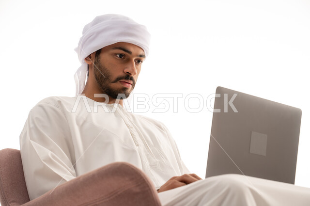 بورتريه لرجل عربي خليجي إماراتي يجلس على كرسي يستخدم جهاز الحاسوب، اجراء مكالمات فيديو، تواصل اجتماعي، محادثات ودردشه، التواصل مع الأصدقاء، اجتماع عمل عن بعد،  تصفح الانترنت ، خلفيه بيضاء .