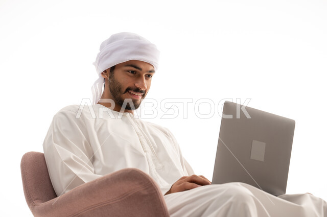 بورتريه لرجل عربي خليجي إماراتي يجلس على كرسي يستخدم جهاز الحاسوب، تصفح الانترنت ، اجراء مكالمات فيديو، تواصل اجتماعي، محادثات ودردشة، التواصل مع الأصدقاء، اجتماع عمل عن بعد،   خلفية بيضاء .