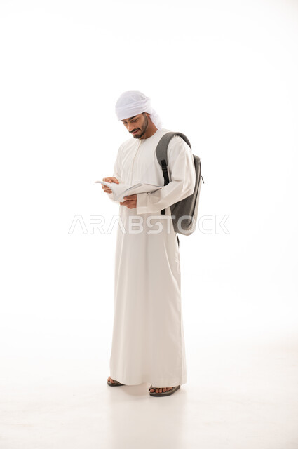 بورتريه لطالب جامعي عربي خليجي اماراتي بالزي الاماراتي التقليدي يحمل حقيبة على ظهره , الذهاب للجامعه ، القراءة والثقافة ,مفهوم التعليم الجامعي ,  صورة الجسم بالطول الكامل , خلفية بيضاء