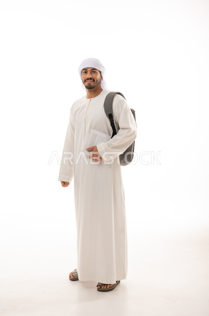 بورتريه لطالب جامعي عربي خليجي إماراتي بالزي الاماراتي التقليدي يحمل حقيبة على ظهره , الذهاب للجامعه ، مفهوم التعليم الجامعي , القراءة والثقافة ,  صورة الجسم بالطول الكامل , خلفية بيضاء