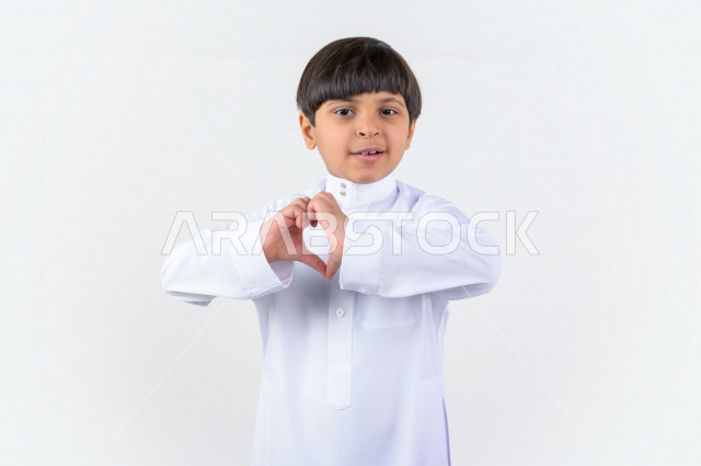 Portrait of a Saudi Arabian Gulf child wearing the Saudi dress, hand gestures indicating the feeling of love, falling in love, happiness and tranquility, love and infatuation, Valentine's Day (Valentine's Day)