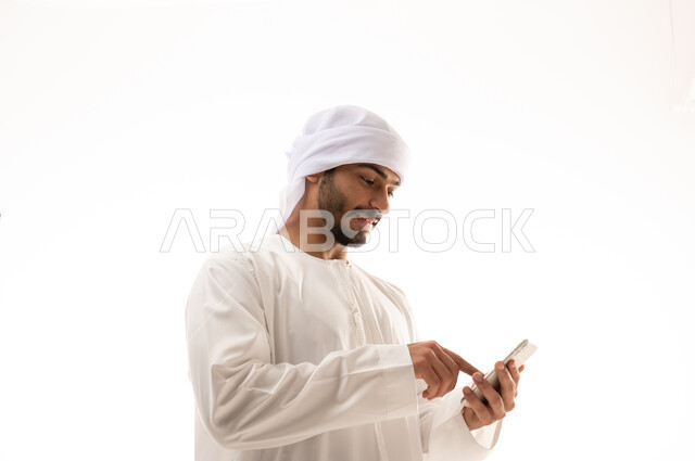 بورتريه  لرجل عربي خليجي إماراتي يرتدي الزي الاماراتي ، استخدام الهاتف المحمول , تواصل اجتماعي، محادثات ودردشة، التواصل مع الأصدقاء، تصفح الانترنت ،  خلفية بيضاء .