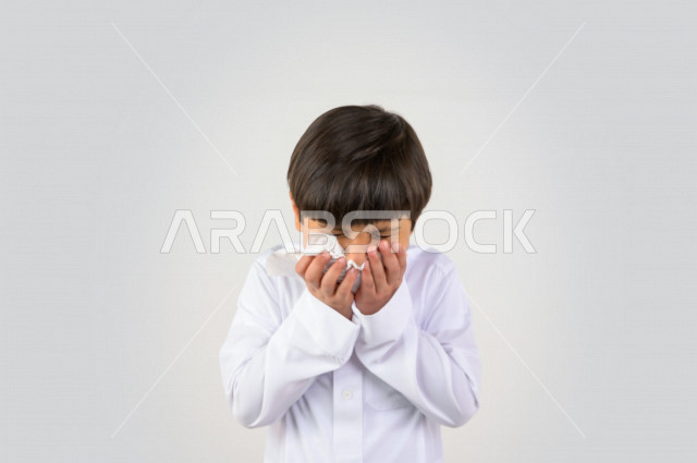 Portrait of a Saudi Arabian Gulf child wearing the Saudi dress, hand and face gestures indicating sneezing, feeling sick, cold, using tissues for sneezing, Corona (Covid_19)