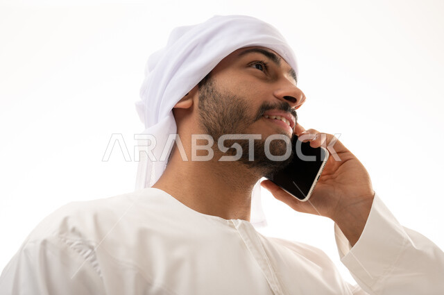 بورتريه  لرجل عربي خليجي إماراتي يرتدي الزي الاماراتي ، استخدام الهاتف المحمول , تواصل اجتماعي ، إجراء مكالمة هاتفية ,  محادثات ودردشة، التواصل مع الأصدقاء،  خلفية بيضاء .