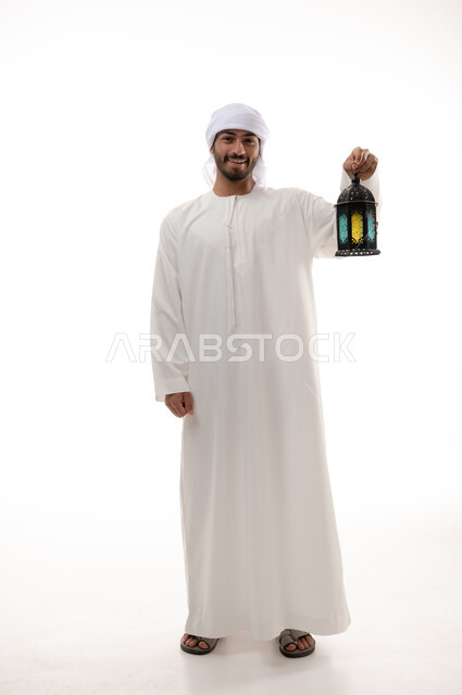 بورتريه لشاب عربية خليجية اماراتي يرتدي الزي الاماراتي التقليدي , يحمل فانوس رمضان ، الإستعداد لقدوم شهر رمضان المبارك ، تحف وديكورات رمضان , المناسبات الدينية والأعياد الإسلامية ، إسلاميات وعبادة ، صورة الجسم بالطول الكامل , خلفية بيضاء .