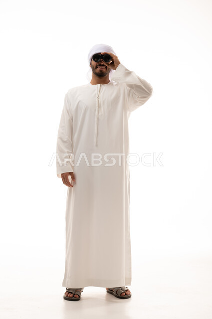 بورتريه لرجل عربي اماراتي خليجي بالزي التقليدي يحمل بيده منظار , يقوم بالنظر من خلال منظار ثنائي العينين  ، التركيز على شيء ما , تلسكوب ,  صورة الجسم بالطول الكامل , خلفية بيضاء .