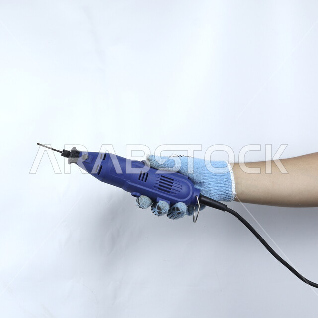 صورة مقربة ليد تمسك مثقب كهربائي مصغر  ,  مقبض بلاستيكي , حفر وتثقيب , ادوات ومعدات اصلاح كهربائية  , خلفية بيضاء .