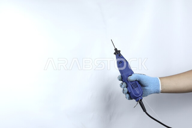 صورة مقربة ليد تمسك مثقب كهربائي مصغر  , ادوات ومعدات اصلاح كهربائية  , مقبض بلاستيكي , حفر وتثقيب , خلفية بيضاء .