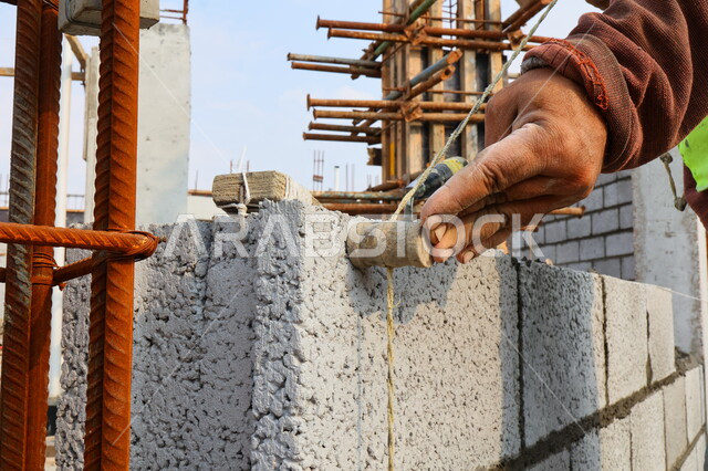صورة مقربة لعامل بناء يقوم ببناء جدار من الطوب والاسمنت، قالب طوبي، اعمال البناء، حائط حجري، ادوات ومعدات البناء