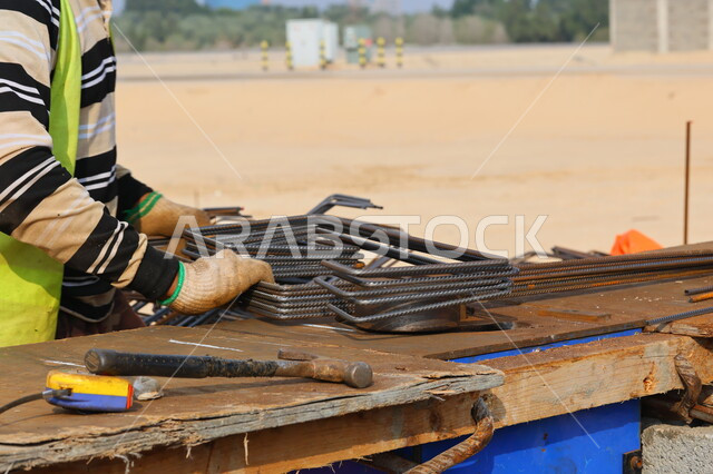 صورة مقربة لعامل بناء يقوم بتجهيز اسياخ البناء المعدنية، عكف وقص الحديد للبناء، معدات وادوات البناء، اعمال البناء، اسياخ معدنية، تركيب الحديد الصلب