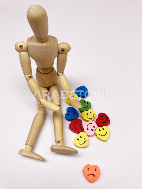 دمية الرجل الخشبي مع مجموعة من الوجوه المبتسمة والحزينة، دما صغيرة على شكل راس قلب، ميداليات، تمثال خشبي، تصاميم واشكال ابداعية، خلفية بيضاء