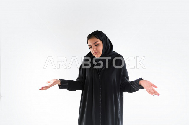 بورتريه لمرأه عربيه سعوديه خليجيه ترتدي العباءة والحجاب , إيماءات يدين تعبر عن قول لا أعلم, عدم المعرفه, الجهل بالأسباب, قلة العلم, الإستفهام عن شيء ما , خلفية بيضاء .