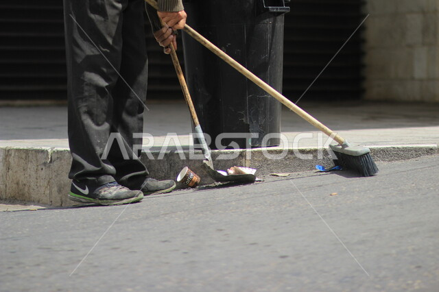 صورة مقربة لعامل النظافة أثناء فترة العمل ، إزالة النفايات  والاهتمام بنظافة البيئة ،أدوات النظافة الخاصة بالعمل , شوارع وطرقات نظيفة . 