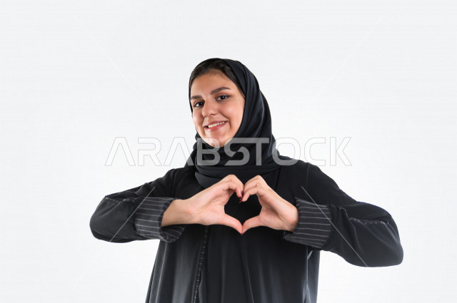 بورتريه لمرأه عربيه سعوديه خليجيه ترتدي العباءة والحجاب , إيماءات يدين تدل على الشعور بالحب, الوقوع في الغرام, السعاده والطمأنينه, المحبه والهيام, عيد الحب ( الفالنتاين) , خلفية بيضاء .