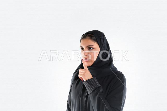 بورتريه لمرأه عربيه سعوديه خليجيه ترتدي العباءة والحجاب , إيماءات يدين تدل على طلب الهدوء, عدم الإزعاج, التوقف عن الكلام, الأمر بالصمت والسكوت , خلفية بيضاء .