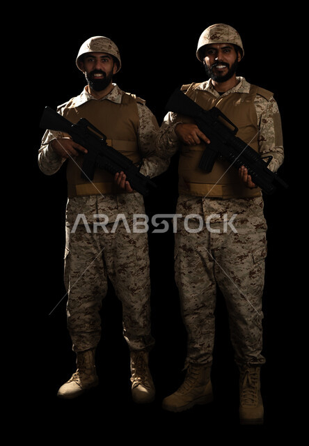 الوقوف بانضباط وحمل السلاح، الدفاع عن الوطن، التدريبات العسكرية والاستعداد للحرب، بورتريه لعسكريان عربيان سعوديان خليجان يرتديان الزي العسكري، القوات المسلحة السعودية، صورة الجسم بالطول الكامل، خلفية سوداء