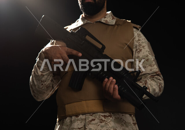 بورتريه مقرب لعسكري عربي سعودي خليجي يرتدي الزي العسكري التقليدي ويقف بانضباط، القوات المسلحة السعودية، حمل السلاح والدفاع عن الوطن، التدريبات العسكرية والاستعداد للحرب، خلفية سوداء