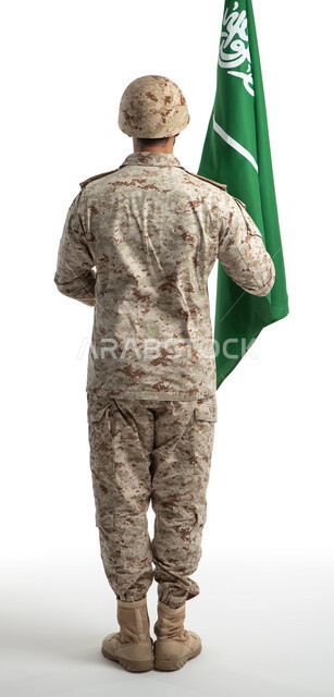 الإحتفال بذكرى اليوم الوطني السعودي 92، بورتريه من الخلف لعسكري عربي سعودي خليجي يحمل العلم السعودي ويقف بانضباط، الدفاع عن الوطن، يوم العلم السعودي، الجيش العربي السعودي، القوات المسلحة السعودية، صورة الجسم بالطول الكامل، خلفية بيضاء