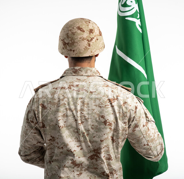 الإحتفال بذكرى اليوم الوطني السعودي 92، يوم العلم السعودي، بورتريه من الخلف لعسكري عربي سعودي خليجي يحمل العلم السعودي ويقف بانضباط، الدفاع عن الوطن، الجيش العربي السعودي، القوات المسلحة السعودية، خلفية بيضاء