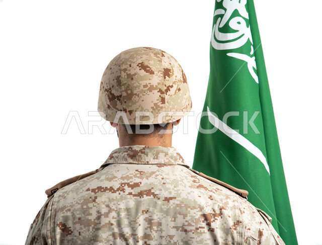 يوم العلم السعودي، بورتريه من الخلف لعسكري عربي سعودي خليجي يحمل العلم السعودي ويقف بانضباط، الدفاع عن الوطن، الإحتفال بذكرى اليوم الوطني السعودي 92، الجيش العربي السعودي، القوات المسلحة السعودية، خلفية بيضاء