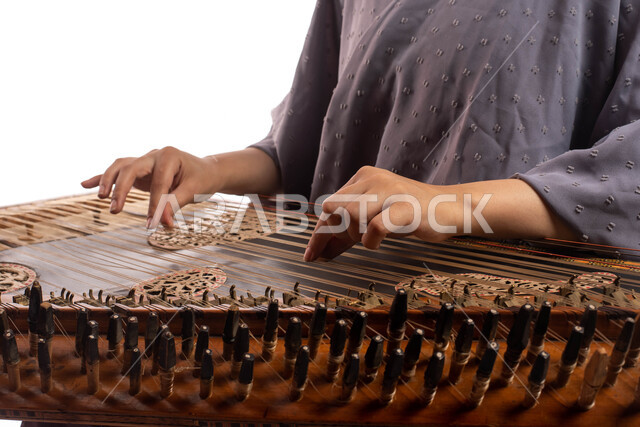 Presenting programs, musical arts and theatrical art, musical artistic talents, close-up portrait of a Saudi Arabian Gulf woman, an artist playing the qanun, using stringed musical instruments, practicing Saudi folk art, white background