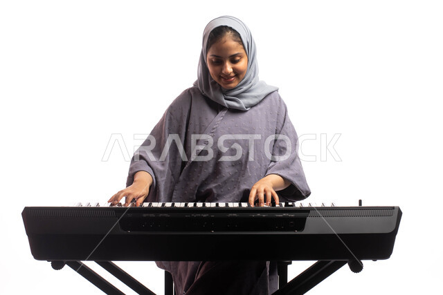 قضاء الوقت بالعزف على آلة البيانو، بورتريه لامرأة خليجية سعودية عربية فنانة تقف امام آلة البيانو الموسيقية ويستمتع بالعزف، مواهب فنية موسيقية، تقديم البرامج والفنون الموسيقية والفن المسرحي، الطرب والانشطة ترفيهية، خلفية بيضاء