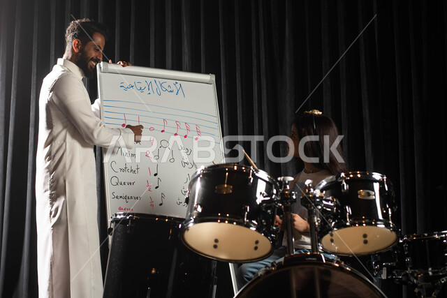 ممارسة هواية الطبل باستخدام آلة الطبل الالكترونية، رجل عربي خليجي سعودي يقوم بتعليم الطفلة على آلة الطبل، جلسات تدريب في الموسيقى، الاشكال الايقاعية الموسيقية، تقديم البرامج والفنون الموسيقية والفن المسرحي، مواهب فنية موسيقية، انشطة ترفيهية