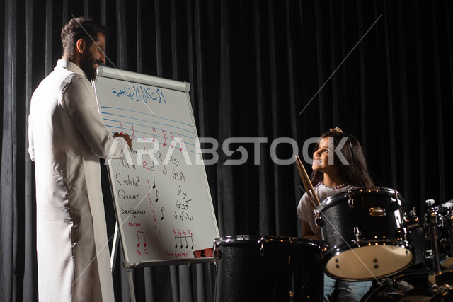 رجل عربي خليجي سعودي يقوم بتعليم الطفلة على آلة الطبل، الاشكال الايقاعية الموسيقية، جلسات تدريب في الموسيقى، ممارسة هواية الطبل باستخدام آلة الطبل الالكترونية، تقديم البرامج والفنون الموسيقية والفن المسرحي، مواهب فنية موسيقية، انشطة ترفيهية