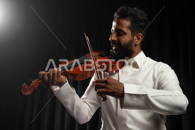 العزف على آلة الكمان، مواهب فنية موسيقية، رجل عازف عربي خليجي سعودي يمارس هواية العزف باستخدام آلة الكمان، تقديم البرامج والفنون الموسيقية والفن المسرحي، استخدام الآلات الموسيقية الوترية، جلسة وناسة وطرب، انشطة ترفيهية