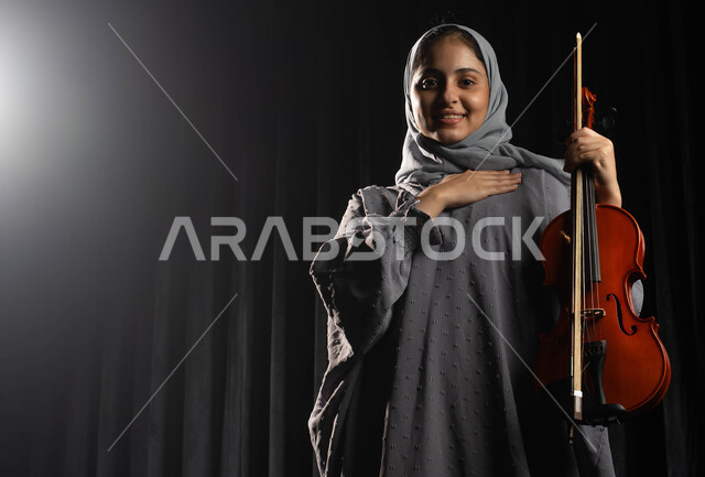 ممارسة هواية العزف على آلة الكمان، امرأة سعودية خليجية عربية فنانة تقوم بالقاء التحية للجماهير على المسرح، استخدام آلة الكمان الوترية في تقديم البرامج والفنون الموسيقية والفن المسرحي، مواهب فنية موسيقية