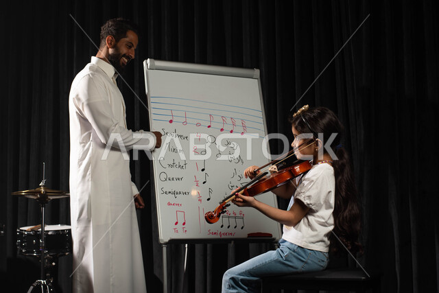 ممارسة هواية العزف باستخدام آلة الكمان الوترية، رجل عربي خليجي سعودي يقوم بتعليم الطفلة على آلة الكمان، النوتات والمقطوعات الموسيقية، جلسات تدريب في الموسيقى، تقديم البرامج والفنون الموسيقية والفن المسرحي، مواهب فنية موسيقية، انشطة ترفيهية