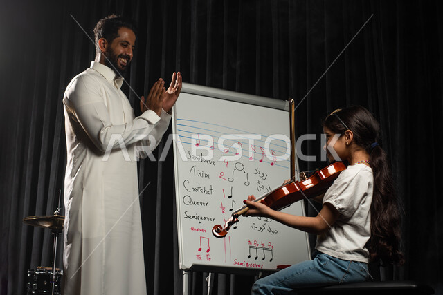 النوتات والمقطوعات الموسيقية، رجل عربي خليجي سعودي يقوم بتعليم الطفلة على آلة الكمان، جلسات تدريب في الموسيقى، ممارسة هواية العزف باستخدام آلة الكمان الوترية، تقديم البرامج والفنون الموسيقية والفن المسرحي، مواهب فنية موسيقية، انشطة ترفيهية