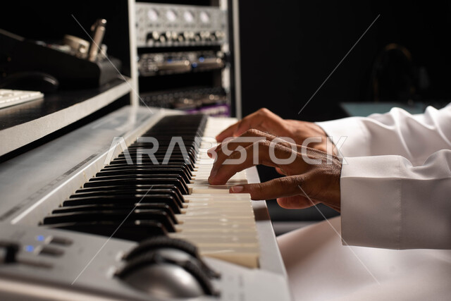 تقديم البرامج والفنون الموسيقية والفن المسرحي، اجهزة تعديل الصوت والموسيقى، مواهب فنية موسيقية، صورة مقربة لرجل خليجي سعودي عربي فنان يجلس امام آلة البيانو الموسيقية ويستمتع بالعزف، قضاء الوقت بالعزف على آلة البيانو