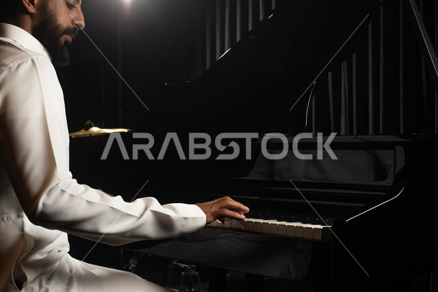 Sitting in front of the piano, a close-up of a Saudi Arabian Gulf man, an artist who spends a good time playing the piano, musical artistic talents, presenting programs, musical arts, theatrical art, rapture and entertainment activities