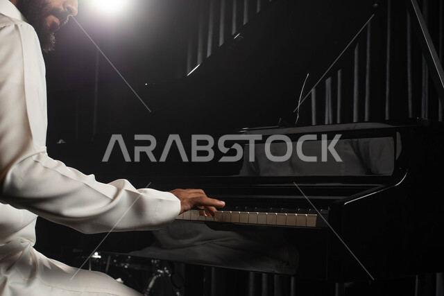 الجلوس امام آلة البيانو الموسيقية، صورة مقربة لرجل خليجي سعودي عربي فنان يقضي وقت ممتع بالعزف على آلة البيانو، مواهب فنية موسيقية، تقديم البرامج والفنون الموسيقية والفن المسرحي، الطرب والانشطة ترفيهية