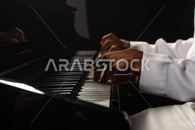 A close-up of a Saudi Arabian Gulf man, an artist sitting in front of the piano instrument and enjoying playing, musical artistic talents, presenting programs, musical arts and theatrical art, spending time playing the piano, singing and entertainment