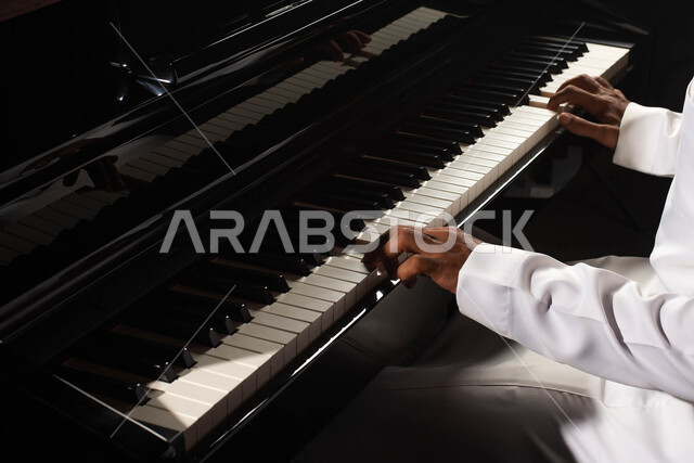 A close-up of a Saudi Arabian Gulf man, an artist sitting in front of the piano instrument and enjoying playing, musical artistic talents, presenting programs, musical arts and theatrical art, spending time playing the piano, singing and entertainment
