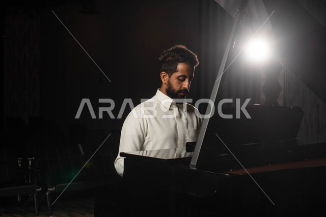 Presenting programs, musical arts and theatrical art, a Saudi Arabian Gulf man, an artist who sits in front of the musical instrument and enjoys playing, musical artistic talents, spending time playing the piano, singing and entertainment activities