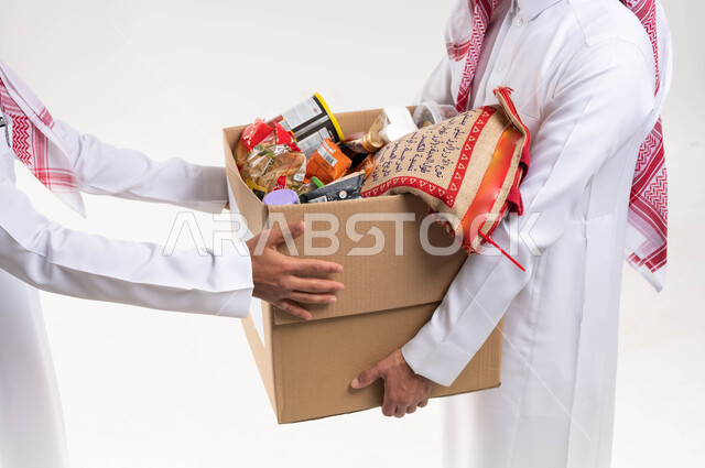 صورة مقربة لرجلان عربيان خليجيان سعوديان يقومان بتجهيز صندوق المواد الغذائية، التبرع لمشروع السلة الغذائية، توفير الطعام للمحتاجين، مبادرات وتبرعات انسانية خيرية، جمعيات اسلامية في السعودية، شهر رمضان، اخراج زكاة الفطر في عيد الفطر المبارك، خلفية بيضاء