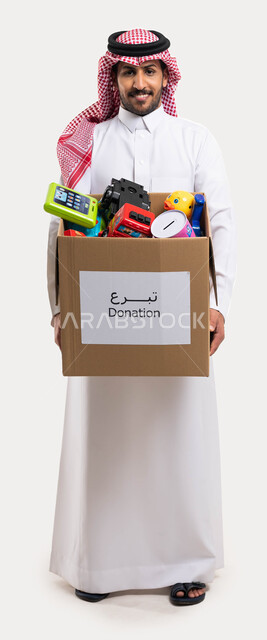 بورتريه لرجل عربي خليجي سعودي يقوم بتوفير الالعاب للاطفال المحتاجين، صندوق تبرعات مليء بالعاب الاطفال، مبادرات وتبرعات انسانية خيرية، جمعيات اسلامية في السعودية، صورة الجسم بالطول الكامل، خلفية بيضاء