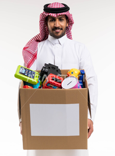 بورتريه لرجل عربي خليجي سعودي يحمل صندوق تبرعات مليء بالعاب الاطفال، توفير الالعاب للاطفال المحتاجين، مبادرات وتبرعات انسانية خيرية، جمعيات اسلامية في السعودية، خلفيه بيضاء
