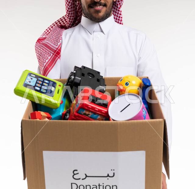 بورتريه مقرب لرجل عربي خليجي سعودي يحمل صندوق تبرعات مليء بالعاب الاطفال، ايماءات وجه مبتسمة، توفير الالعاب للاطفال المحتاجين، مبادرات وتبرعات انسانية خيرية، جمعيات اسلامية في السعودية، خلفيه بيضاء