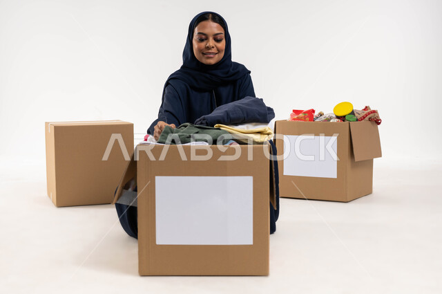 بورتريه لامرأة عربية خليجية سعودية تقوم بترتيب ملابس وهدايا العيد السعيد، جمع وتوزيع صناديق التبرعات للمحتاجين، مبادرات وتبرعات انسانية خيرية، جمعيات اسلامية في السعودية، خلفية بيضاء