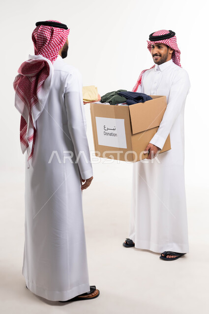 جمعيات خيرية ومبادرات انسانية ، بورتريه لرجلان  خليجيان سعوديان عربيان  يتشاركان في تجهيز صندوق تبرعات الملابس الفائضه ، اهداء ملابس العيد للمحتاجين ، خدمة المجتمع السعودي المتعفف، صورة الجسم بالطول الكامل ، خلفية بيضاء.