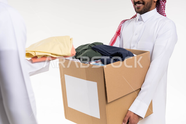 بورتريه لرجلان سعوديان عربيان خليجيان   يتشاركان في تجهيز صندوق تبرعات الملابس الفائضه ، اهداء ملابس العيد للمحتاجين ، جمع وتوزيع التبرعات خيرية ،جمعيات خيرية ومبادرات انسانية  ، خدمة المجتمع السعودي المتعفف، خلفية بيضاء.